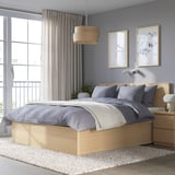 Camera da letto moderna con letto MALM, struttura in legno chiaro, lenzuola grigie. Decorato con arte minimalista, ampia finestra e luce naturale. Tappeto e lampada accanto.