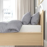 Letto accogliente con cuscini grigi e coperta, testiera in legno, vicino alla finestra.