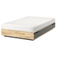 Un letto MANDAL in legno naturale con materasso bianco. Ha un design semplice e rettangolare con linee pulite.