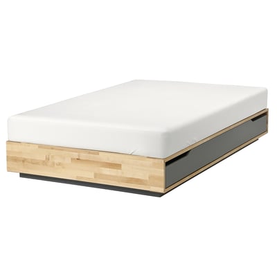 Un letto MANDAL in legno naturale con materasso bianco. Ha un design semplice e rettangolare con linee pulite.