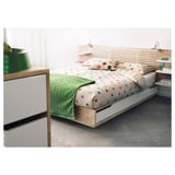 Scena moderna della camera da letto con letto MANDAL, biancheria da letto a pois colorati, testiera in legno e cassetti portaoggetti, coperta verde e pavimenti grigi a spina di pesce.
