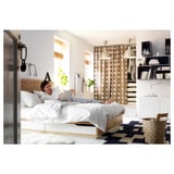 Una donna si rilassa su un letto di legno bianco con cassetti, usando un laptop. La stanza è dotata di una tenda a pois, di un cesto intrecciato e di scaffali con oggetti decorati.