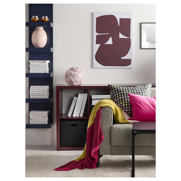 Soggiorno moderno con libreria in legno scuro, divano grigio, plaid colorato e arte astratta.