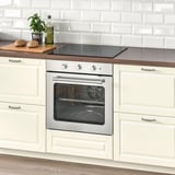 Cucina moderna con forno argento, armadi bianchi, piano cottura nero. Il bancone ha pane, piante, olio d'oliva. Alzatina in stile mattone.