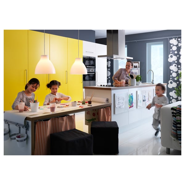 Tre bambini in cucina: due che bevono, uno vicino alla tenda; armadi gialli, luci moderne.