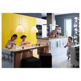Tre bambini in cucina: due che bevono, uno vicino alla tenda; armadi gialli, luci moderne.