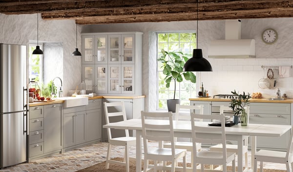 Cucina moderna con armadi grigio chiaro, ripiani in legno, elettrodomestici in acciaio inossidabile, set da pranzo bianco, illuminazione sotto il mobile e una grande finestra.