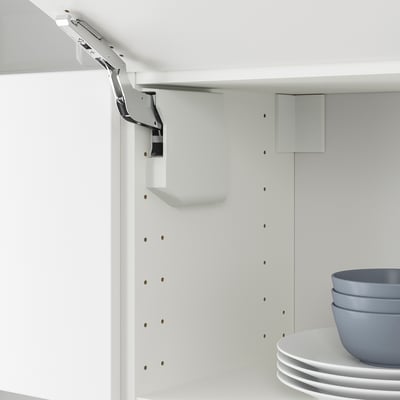 Mobile da cucina bianco con meccanismo di sollevamento della porta veddinge mostrato, incluso il fermo per una chiusura delicata. Ciotole e piatti impilati su ripiano.