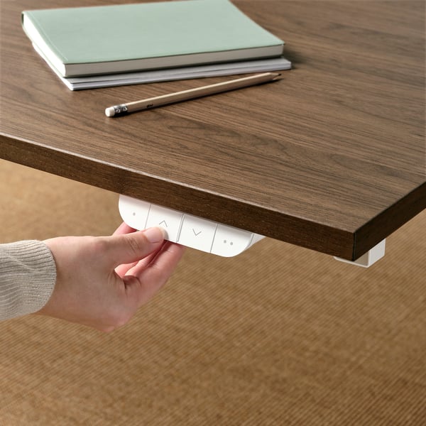 L'immagine mostra una mano che regola i comandi sotto una scrivania di legno, probabilmente per la regolazione dell'altezza.