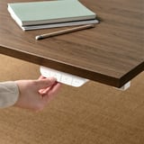 L'immagine mostra una mano che regola i comandi sotto una scrivania di legno, probabilmente per la regolazione dell'altezza.
