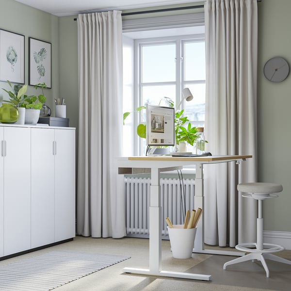 Home office verde e luminoso con scrivania sit-stand bianca MITTZON vicino alla finestra, sedia e armadietto.