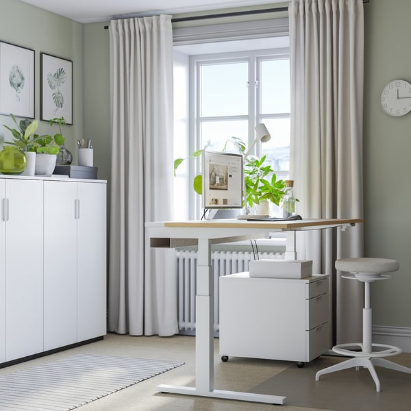 Moderno ufficio domestico con scrivania bianca MITTZON sit/stand. Design pulito, sedia ergonomica, ampia finestra e armadietto.