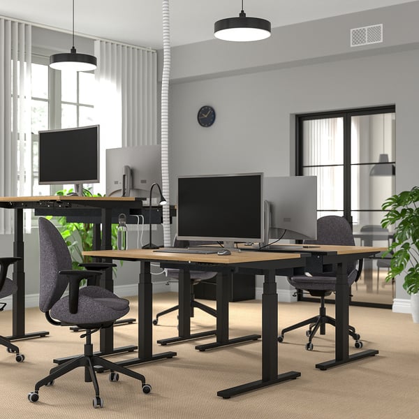 Ufficio moderno con scrivanie sit-stand nere MITTZON, design elegante, piani in legno, sedie grigie, computer e pareti bianche, che uniscono tecnologia e comfort.