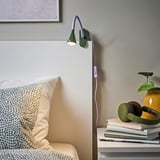 Accogliente camera da letto con lampada viola-verde, comodino, libri, cuffie, piante.