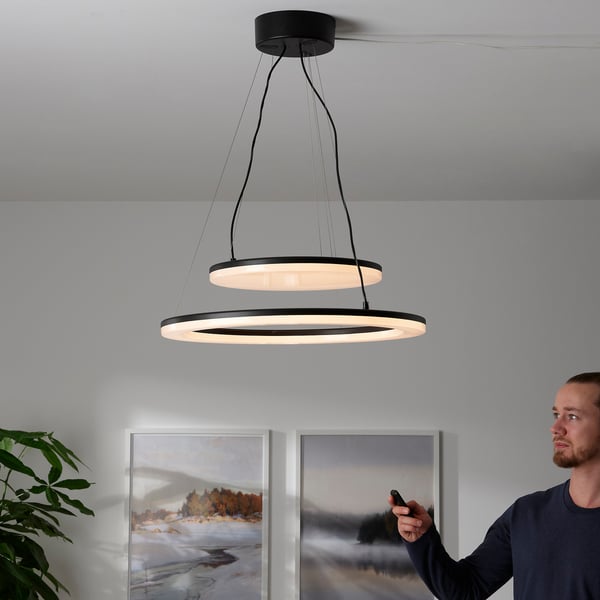 Uomo che regola la moderna lampada a sospensione a doppio anello con telecomando, controllo della luminosità e del posizionamento.