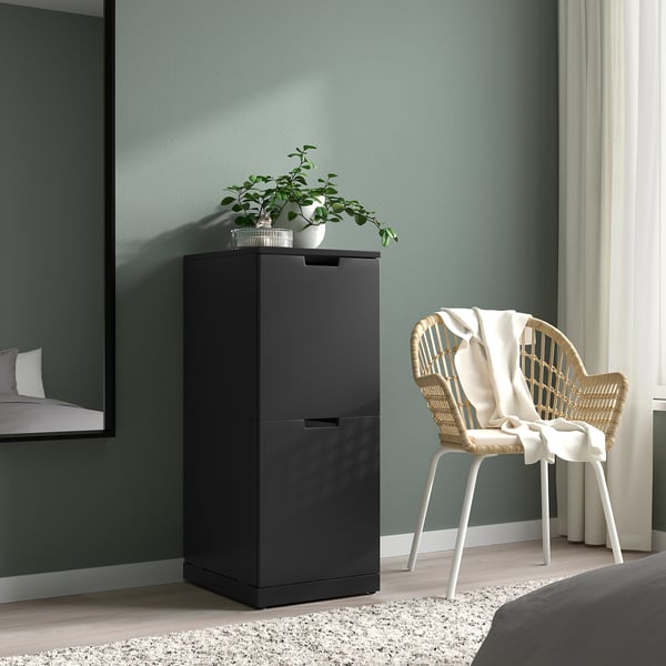 Camera da letto moderna con cassapanca NORDLI nera, sedia in vimini e pianta.