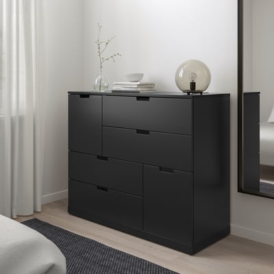 Cassapanca NORDLI nera con lampada, libri e vaso in camera minimalista.