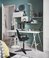 Moderno spazio di lavoro domestico con sedia girevole ODGER bianca, pareti verde acqua, lampada da scrivania nera, scaffali con libri e un orologio.