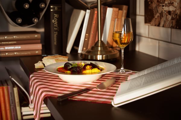 Accogliente pasto a base di pesce con vino e libri sul tavolo scuro.