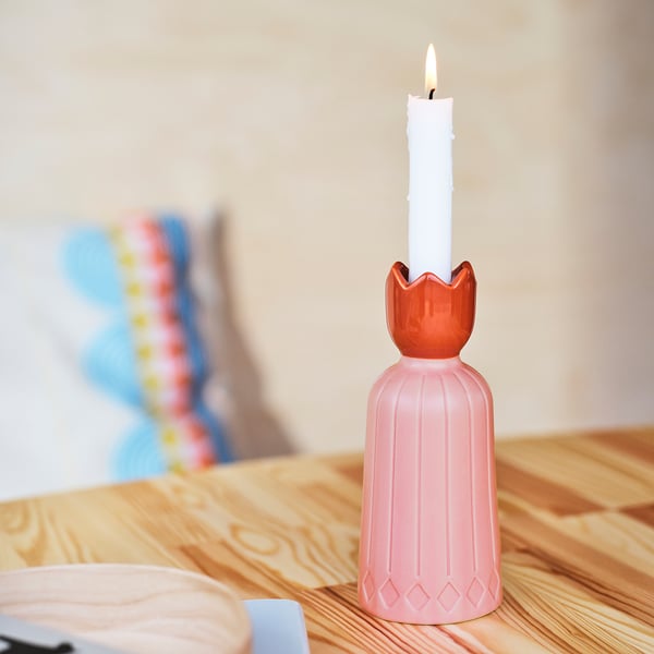 Una candela accesa in un portacandele rosa a forma di fiore, posta su un tavolo di legno.