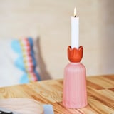 Una candela accesa in un portacandele rosa a forma di fiore, posta su un tavolo di legno.