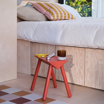 Sgabello triangolare in pino rosso con candela e oggetti sotto il letto.