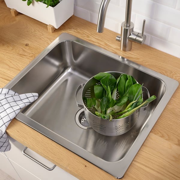 Lavello in acciaio inox con scolapasta pieno di verdure verdi sul bancone.