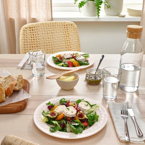 Tavola apparecchiata con piatti da insalata bianchi, bicchieri, posate, pane e caraffa. Stoviglie decorative e resistenti in vetro temperato.