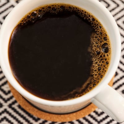 La tazza da caffè bianca riempita con caffè tostato scuro si trova sopra una coperta a motivi bianchi e neri.