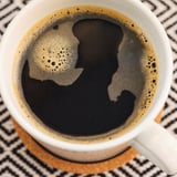 Tazza in ceramica bianca con caffè nero e schiuma d'arte su un sottobicchiere.