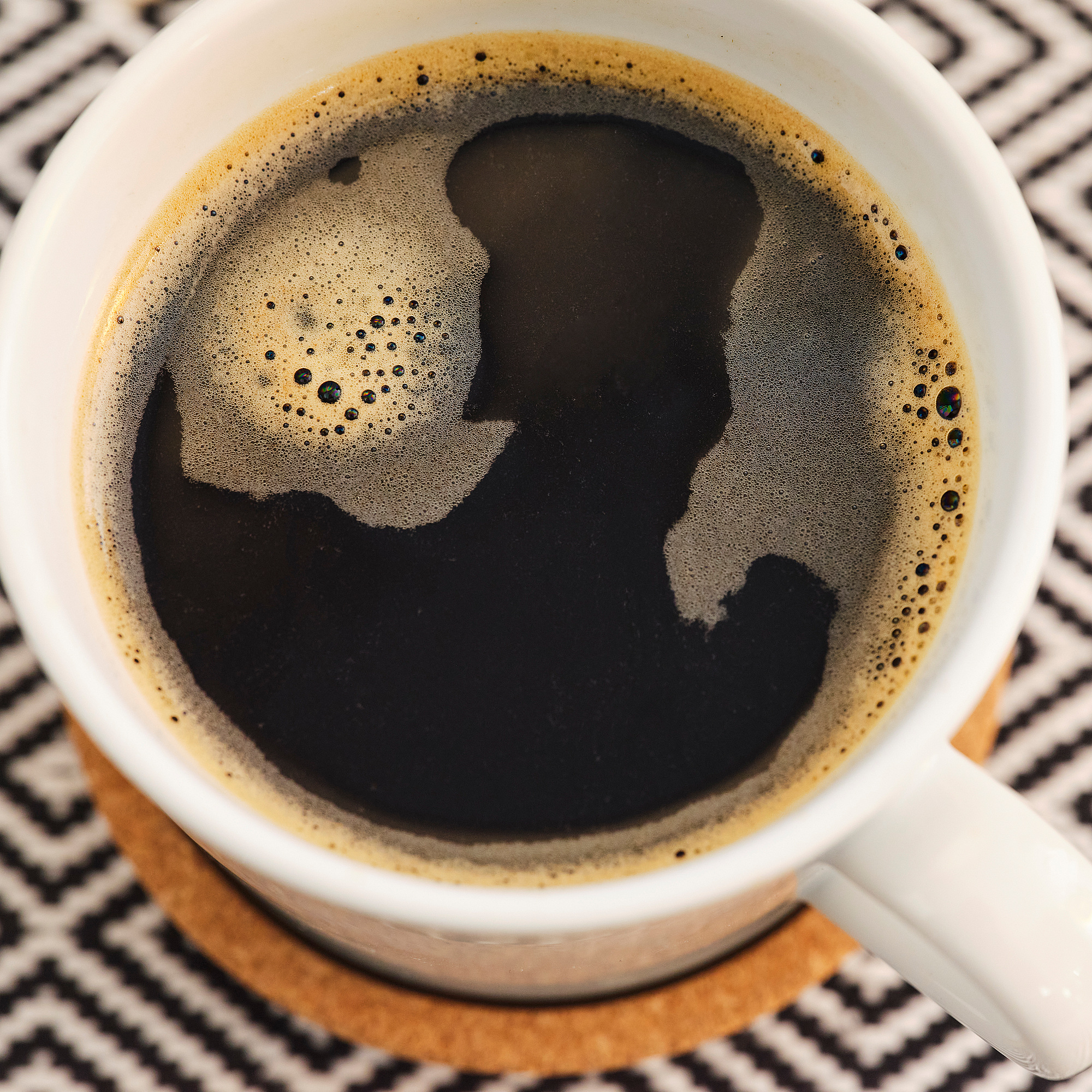Tazza in ceramica bianca con caffè nero e schiuma d'arte su un sottobicchiere.