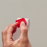 Inserire a mano una spina di sicurezza PATRULL rossa in una presa a muro.