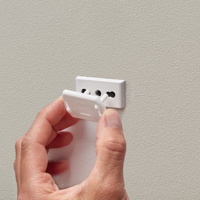 Spina di sicurezza bianca che tiene la mano accanto alla presa a muro, progettata per bloccare l'accesso alla presa.