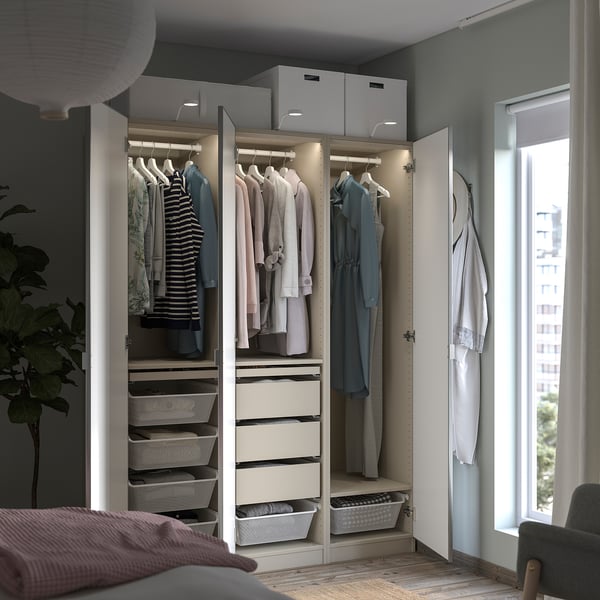 Camera da letto moderna con armadio PAX bianco. Contiene vestiti, cestini, cassetti e ha un'illuminazione integrata.
