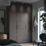 Camera da letto moderna con armadio PAX grigio, sedia bianca e piante verdi vicino alla finestra.