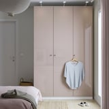 Camera da letto moderna con grande armadio PAX beige, letto grigio e cesto di vimini sotto una lampada a sospensione.