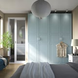 Camera da letto moderna con armadi PAX blu-grigi, luci calde e indumenti visibili.