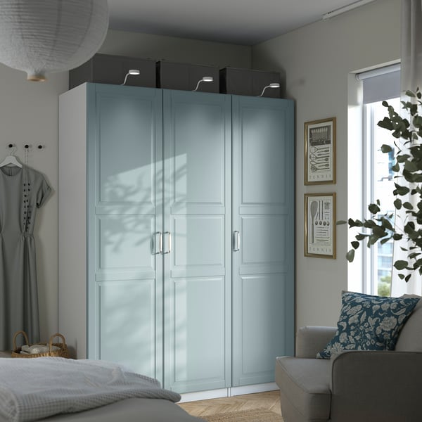 Camera da letto moderna con alto armadio PAX blu, porte in vetro, indumento appeso e decorazioni.