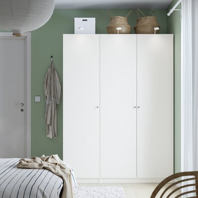 Camera da letto moderna con armadio PAX bianco alto, cestini, sciarpa, letto e sedia.