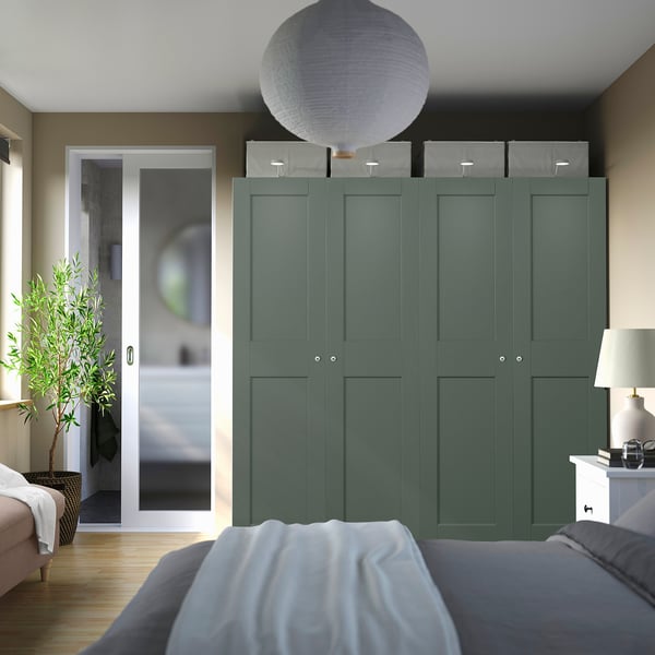 Camera da letto moderna con grande armadio verde acqua, scatole grigie e porta del bagno aperta. Letto in primo piano.