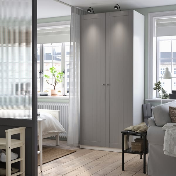Camera da letto moderna con armadio PAX grigio alto, scrivania e divano grigio.