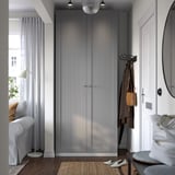 Ingresso moderno con grande armadio grigio PAX, appendiabiti e una piccola poltrona bianca vicino alla finestra. L'armadio è grande, alto e snello.
