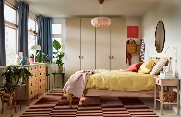 Camera da letto luminosa con letto giallo, cassettiera in legno, tende blu, luci rosa e piante.