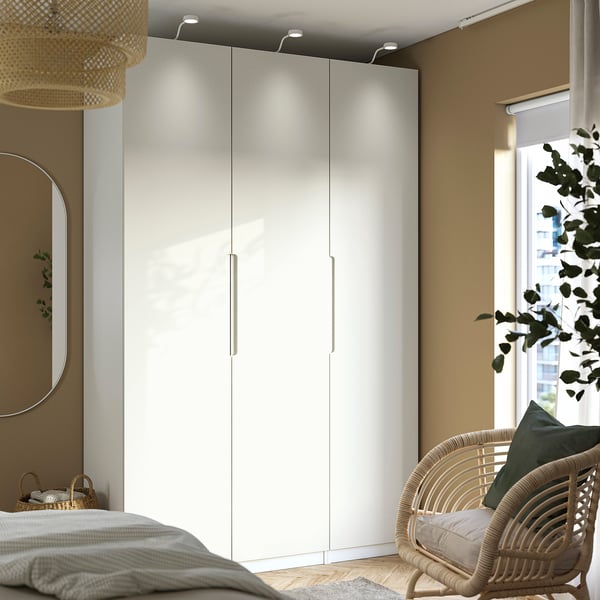 Camera da letto moderna con armadio PAX alto, specchio rotondo, sedia in vimini e grande finestra.