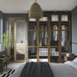 Camera da letto moderna con armadio alto in legno scuro PAX, pannelli in vetro, porta scorrevole in legno chiaro, lampada a sospensione e letto a righe.