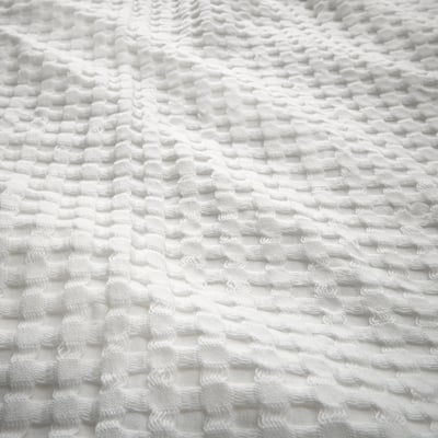 Un copriletto bianco, quadrato e reversibile, realizzato in cotone con texture waffle.