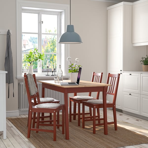 Piccolo set da pranzo in legno rosso con sedie imbottite, centrato sotto una grande luce, accanto ai mobili della cucina.