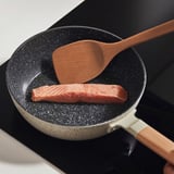 Padella con spatola di legno e carne cruda. Antiaderente, distribuzione uniforme del calore, adatto a tutti i piani cottura.