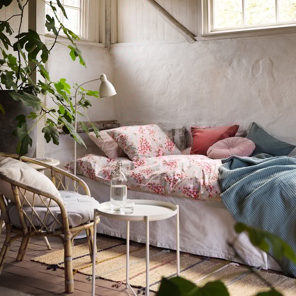 Camera accogliente e rustica con letto floreale, cuscini rosa, sedia in vimini, altrove, tappeto RAKLEV - colorato, tessuto misto iuta/lana, morbido, terroso.