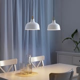 Lampade a sospensione sopra il tavolo da pranzo con caraffa. Le tende blu lasciano entrare la luce.